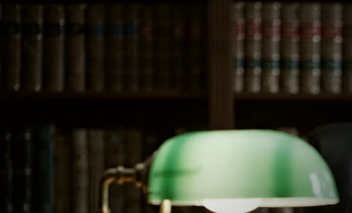 Estante com livros e luminária de mesa de cúpula verde.