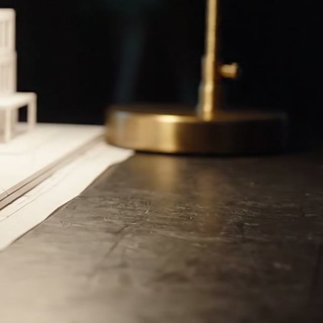 Base de latão de uma luminária sobre um tampo de pedra escura, ao lado de uma maquete