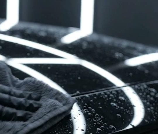 Capô preto com gotas de água e reflexos das luzes do estúdio, sendo seco com toalha de microfibra