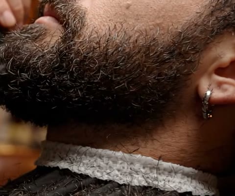 Perfil de um cliente de barba cheia, com a golinha de papel no pescoço