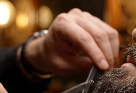Mão do barbeiro, de relógio no pulso, segurando o pente junto à barba