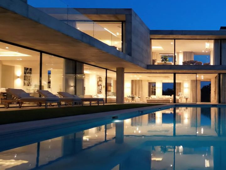 Espreguiçadeiras ao lado da piscina, diante de uma sala com paredes de vidro