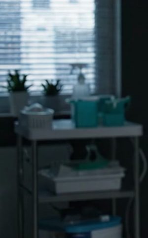 Janela com persiana, vasos de plantas e carrinho com materiais de atendimento